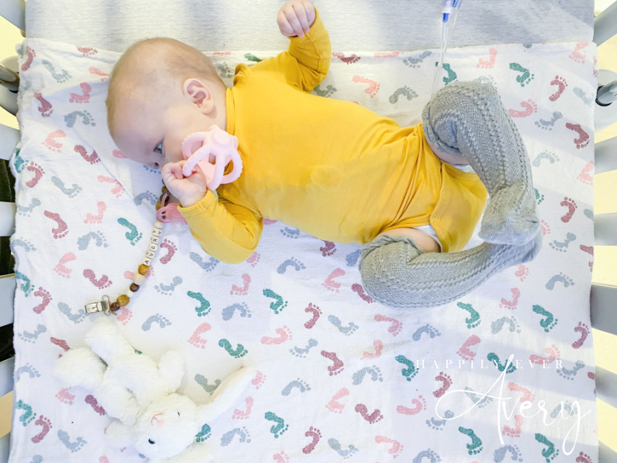 infant in yellow sleeper with teether laying in hospital crib